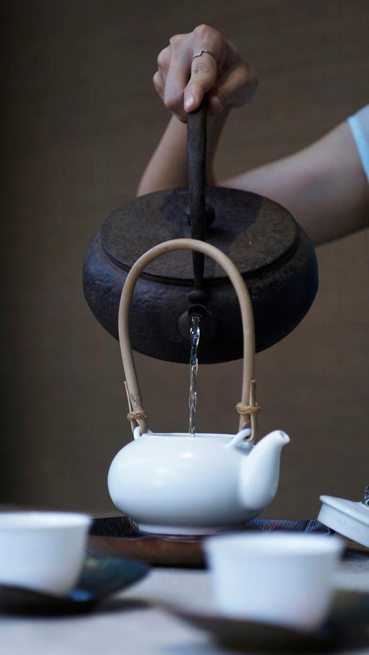 person pouring water on ceramic teapot