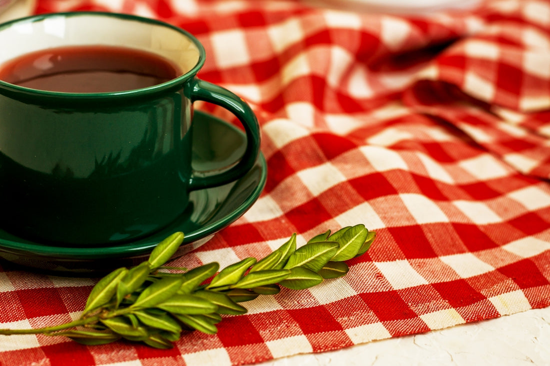 a cup of tea and a green leaf on a red and white checkered table