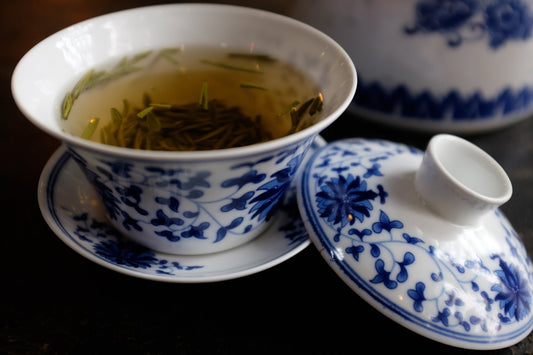 A cup of green tea next to a tea pot